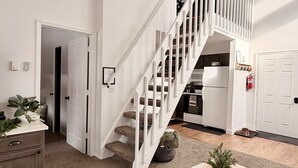 A spacious living area with a white staircase, a wooden coffee table, and a kitchen in the background. - Cozy Condo -Walk to Downtown McCall & Marina! Hot Tub, Indoor Pool, Sauna &more. (McCall)