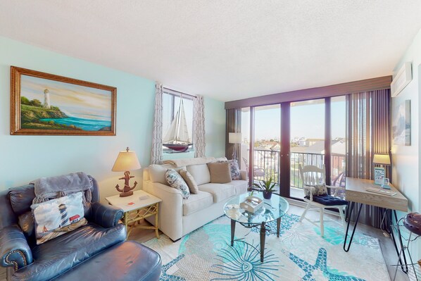 A modern living room with a sofa, a glass coffee table, and a view of the sea through large windows.