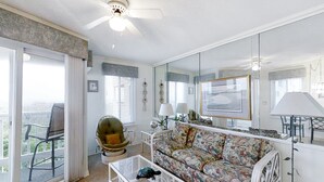 A living room with a sofa, a glass coffee table, a chair, a ceiling fan, and a large mirror.