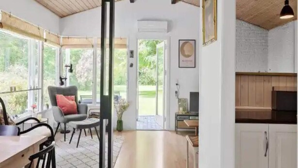 A spacious room with a high ceiling, a dining area with a table and chairs, a seating area with a chair and a sofa, and a kitchen area with cabinets and a countertop. - 5 Star Holiday Home in Jaegerspris (Melby)