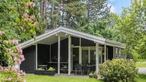 A small, single-story building with a covered patio area, surrounded by lush greenery. - 5 Star Holiday Home in Jaegerspris (Melby)