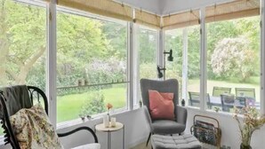 A sunroom with large windows, a chair, a small table, and a view of a garden. - 5 Star Holiday Home in Jaegerspris (Melby)