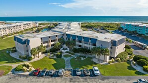 Ein mehrstöckiges Hotel mit Parkplatz, Pool und Meerblick.