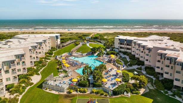 Ein Resort mit einem zentral gelegenen Pool, umgeben von Liegebereichen und Blick auf den Strand.