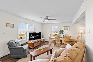 A living room with a television, a sofa, a dining table with chairs, and a ceiling fan. - RG & Carole's Place: Updated beach cottage with enclosed patio, 2 decks, grill, AC, & W/D (Atlantic Beach)