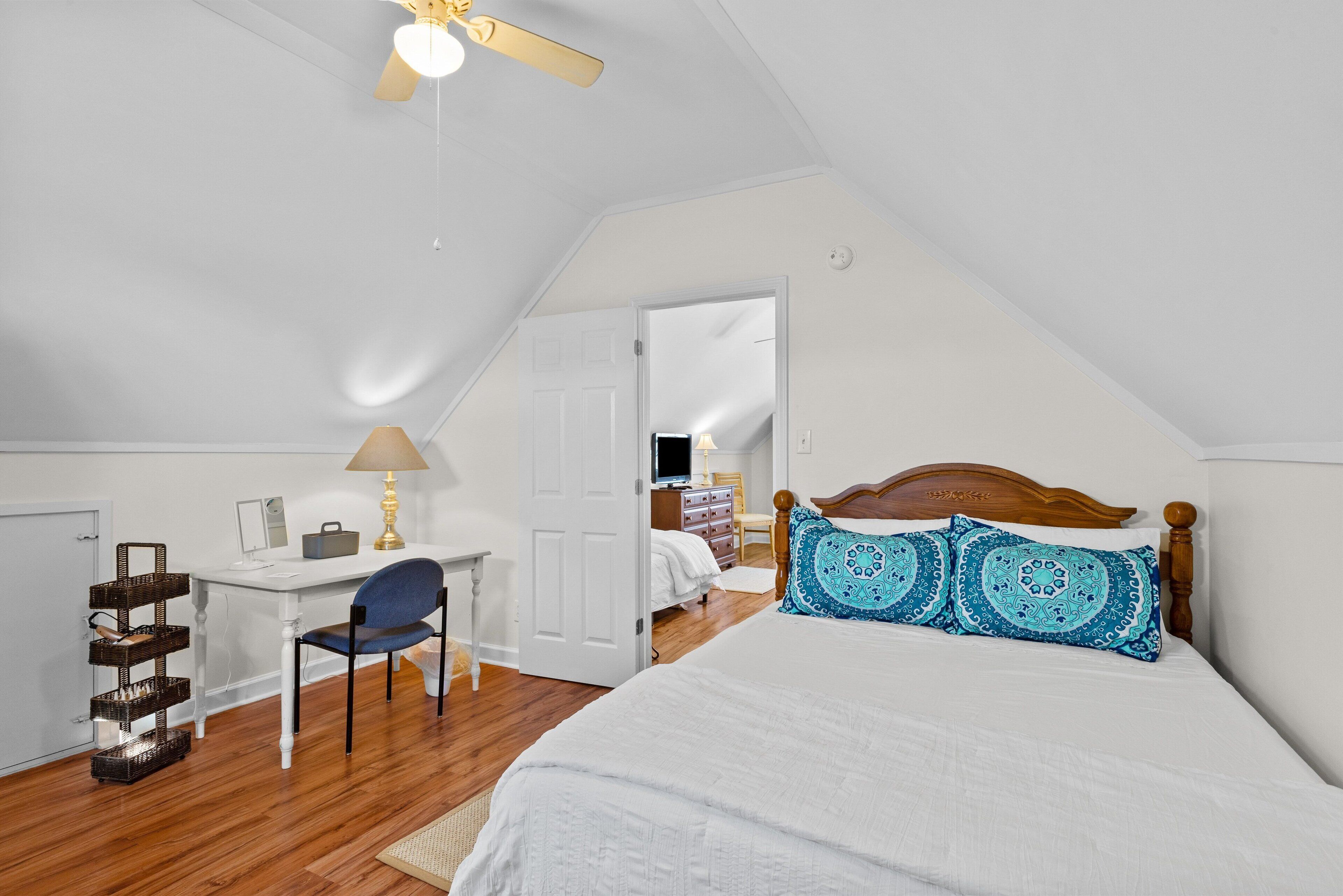 Un dormitorio con una cama, un escritorio, una silla y un ventilador de techo.