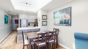 Una cocina moderna con armarios blancos, una isla central y un comedor con sillas de madera.