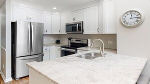 Una cocina moderna con armarios blancos, electrodomésticos de acero inoxidable, encimera de granito y un reloj de pared.
