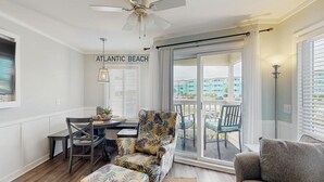 A living room with a ceiling fan, a dining table with chairs, a patterned armchair, a sofa, and a view of the outside. - First-Floor Condo with Balcony, WiFi & Shared Hot Tub, Pools, Tennis, Putt-Putt (Atlantic Beach)