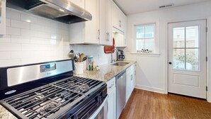 A modern kitchen with white cabinets, a stainless steel range hood, a built-in dishwasher, and a granite countertop. - Dog-friendly cottage across from the water in a walkable neighborhood (Beaufort)