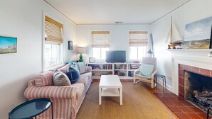 A living room with a striped sofa, a white coffee table, a bookshelf, a fireplace, and a television. - Dog-friendly cottage across from the water in a walkable neighborhood (Beaufort)