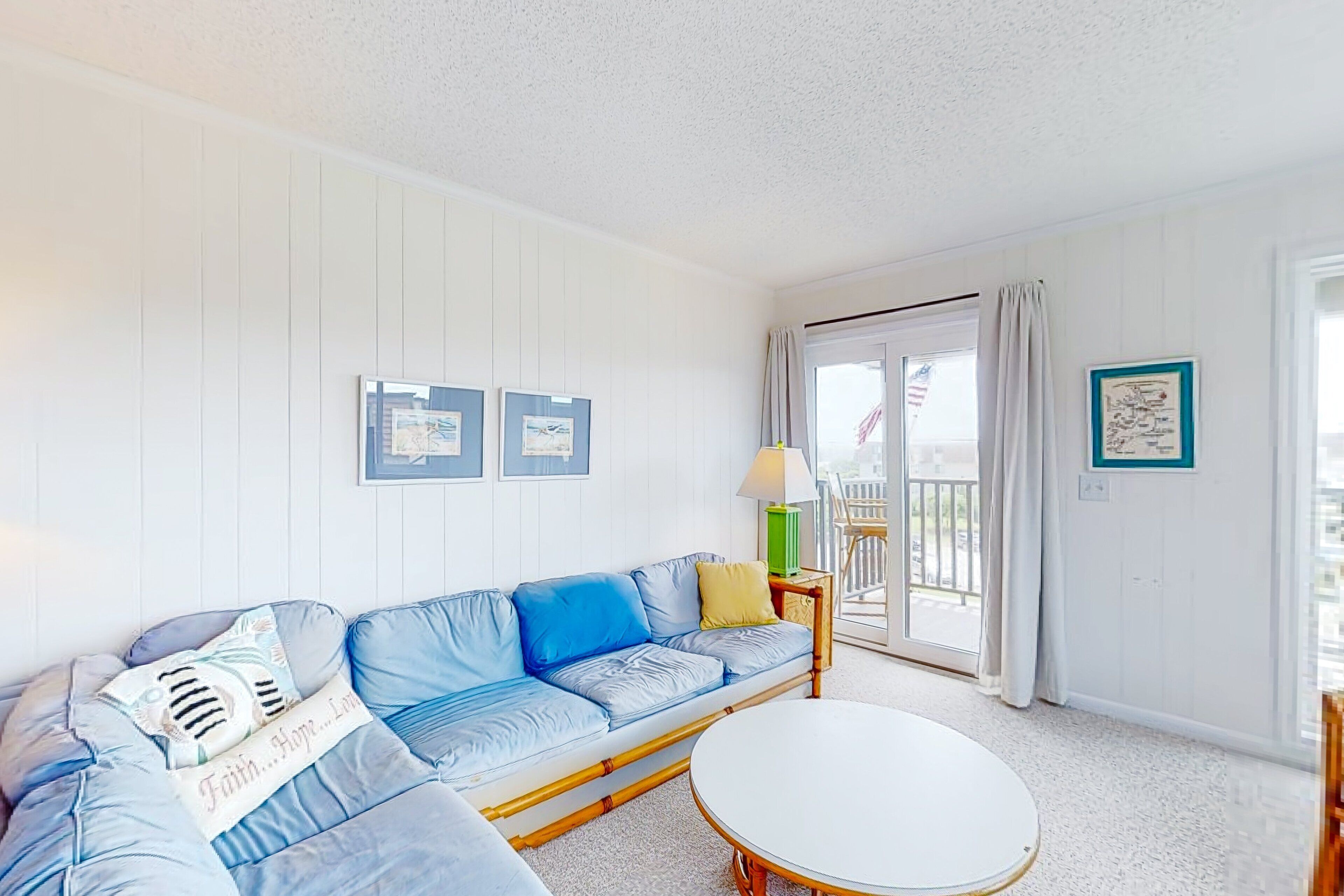 Una habitación con un sofá azul, una mesa redonda blanca y vistas al exterior a través de una puerta corrediza de vidrio.