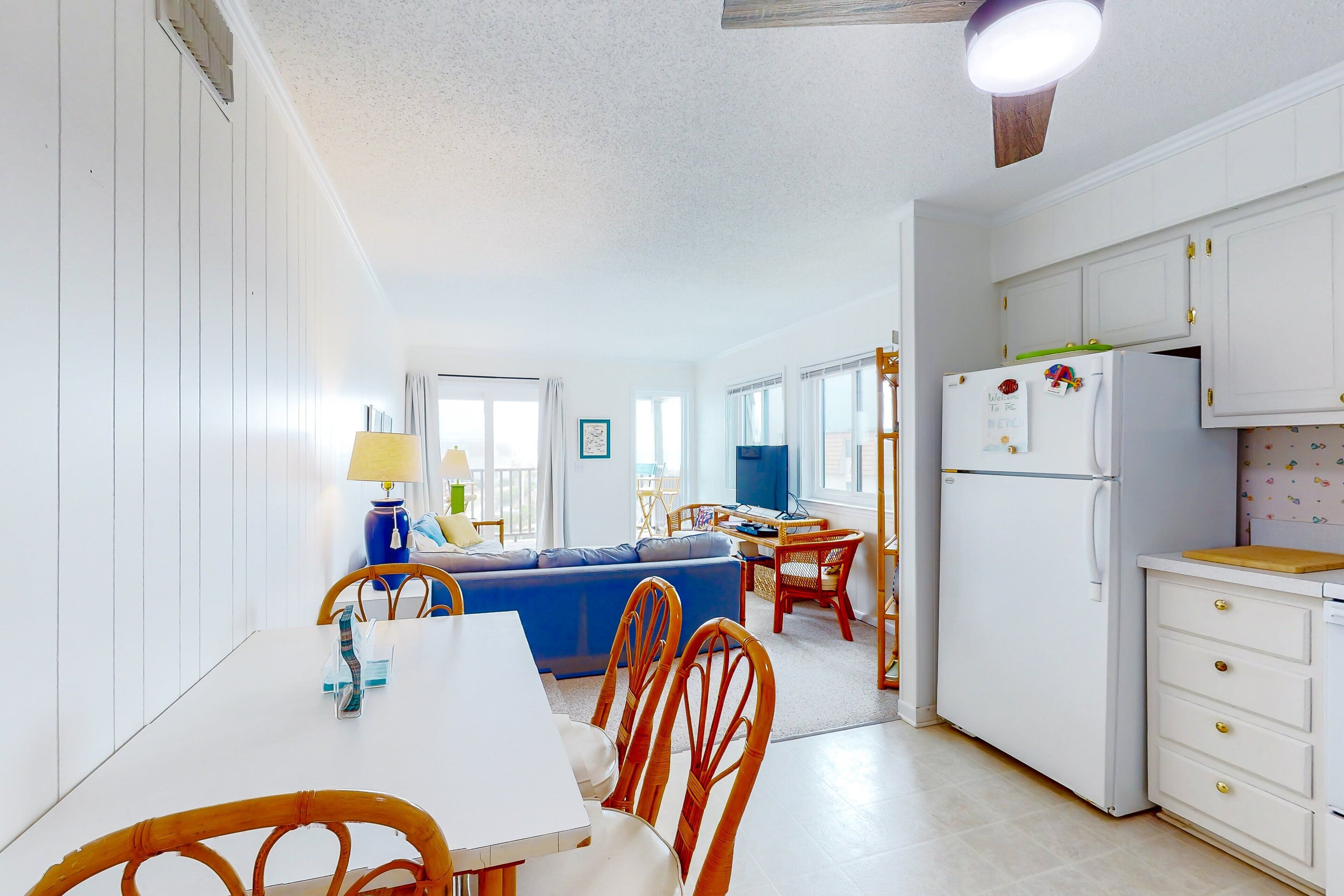 A compact kitchen with white cabinets, a dining table with chairs, and a blue sofa in the background.