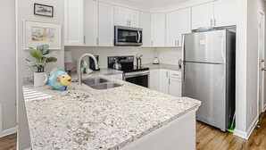 Een moderne keuken met witte kastjes, roestvrijstalen apparatuur, een granieten aanrecht en een decoratief beeld van een vis.