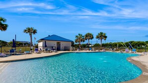 A clear blue swimming pool with lounge chairs and a building in the background. - Ocean view condo with shared pool, fitness room, & balcony (Indian Beach)
