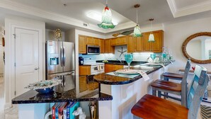 A modern kitchen with stainless steel appliances, wooden cabinets, and a central island with seating. - Ocean view condo with shared pool, fitness room, & balcony (Indian Beach)