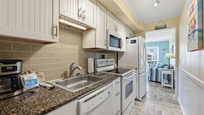 Una cocina con armarios blancos, microondas, refrigerador, cafetera y pileta.