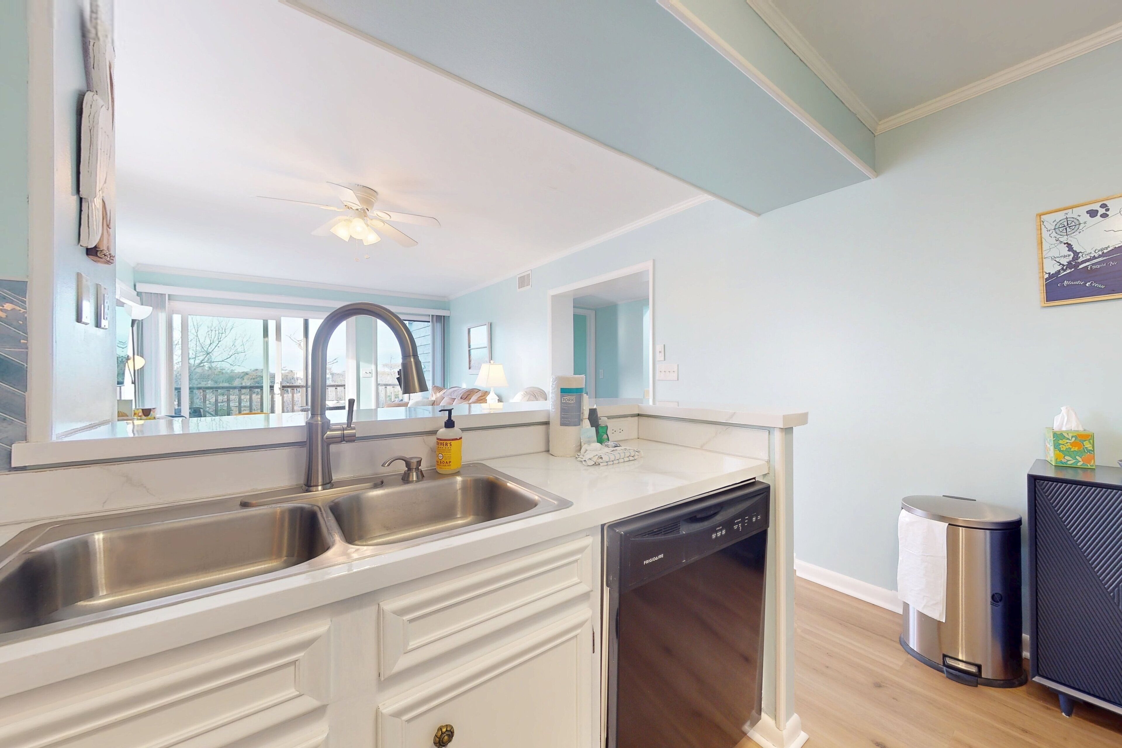 A kitchen with a double sink, dishwasher, and a trash can.