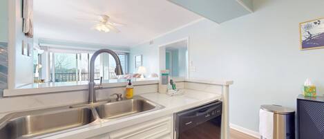 A kitchen with a double sink, dishwasher, and a trash can.