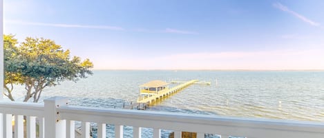 A waterfront view with a pier extending into the water, a white railing, and a tree on the left.