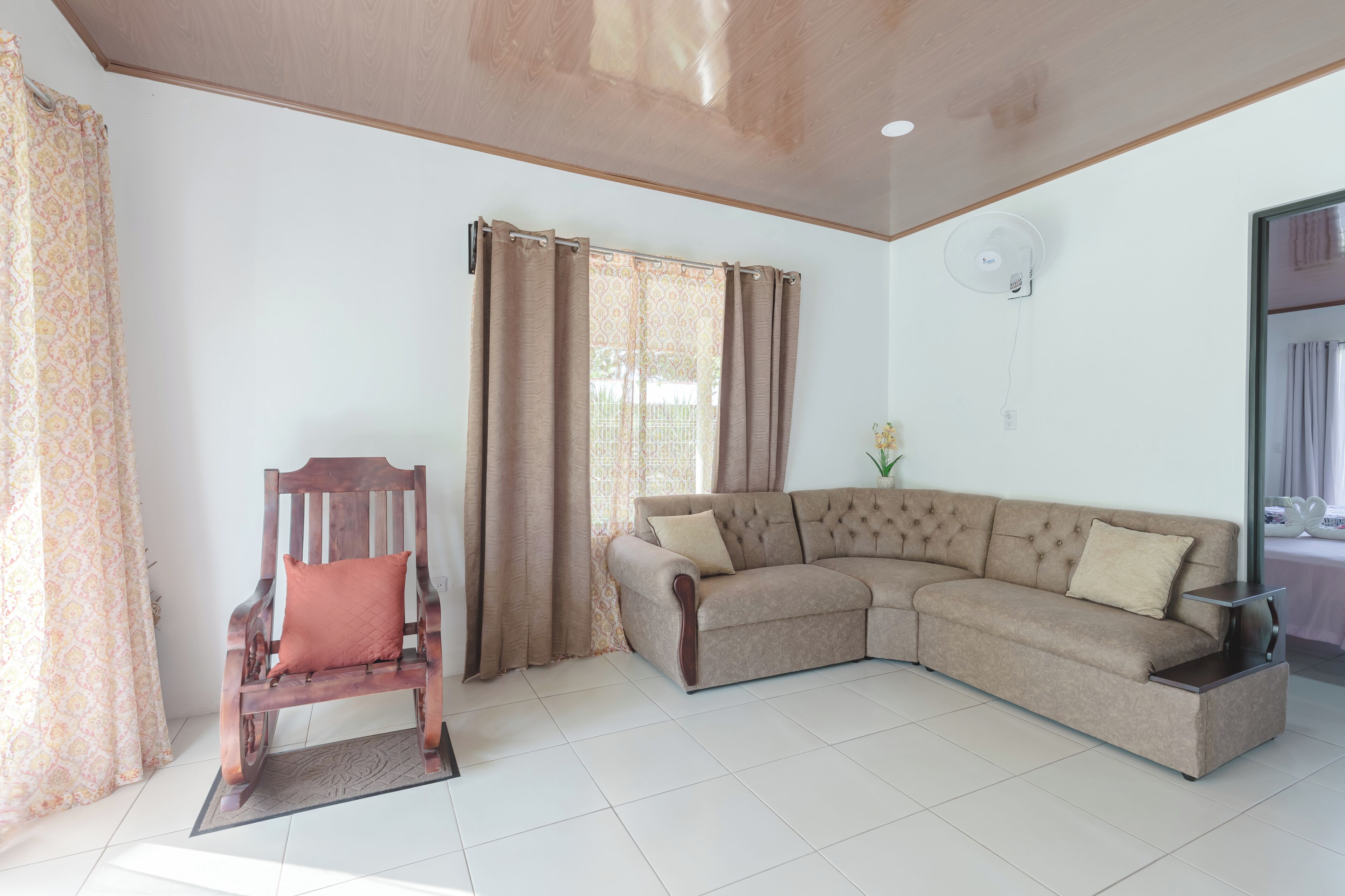 A living room with a sectional sofa, a wooden rocking chair, and a window with curtains.