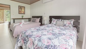 Habitación de hotel con dos camas, una mesita, una planta en maceta y un cuadro en la pared.