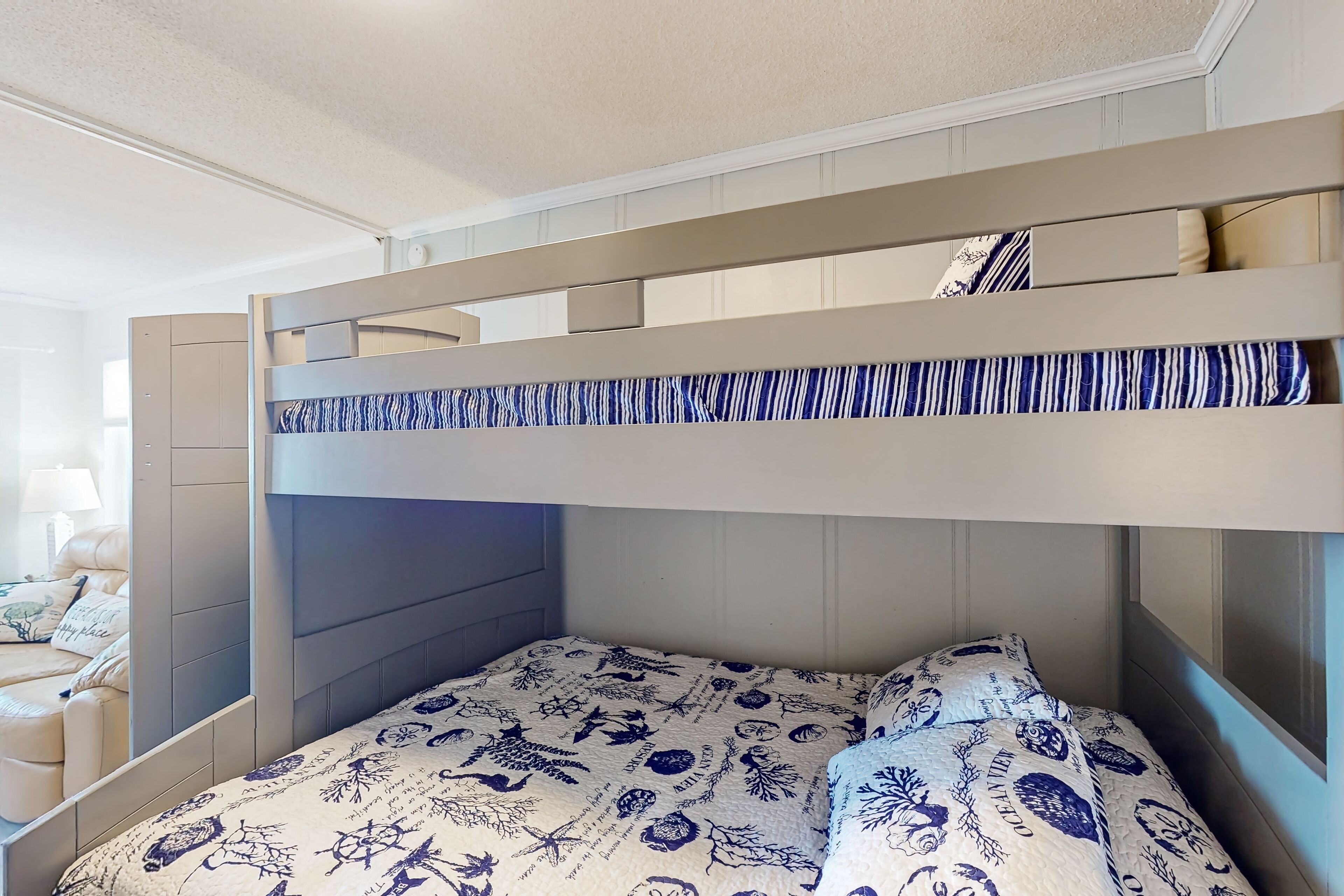 A bunk bed with a patterned bedspread, a headboard, and a nightstand with a lamp.
