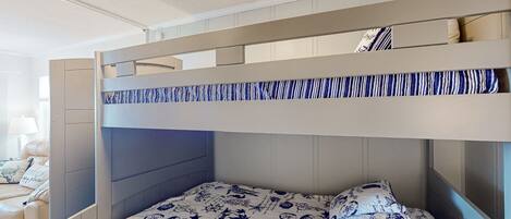A bunk bed with a patterned bedspread, a headboard, and a nightstand with a lamp.