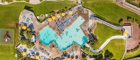 An aerial view of a resort with a large pool, sun loungers, and a water slide.