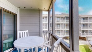 Un balcon avec une table et des chaises blanches, donnant sur un immeuble doté de nombreux balcons.