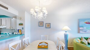 Un comedor con una mesa blanca, sillas, una araña, una lámpara y un cuadro en la pared.