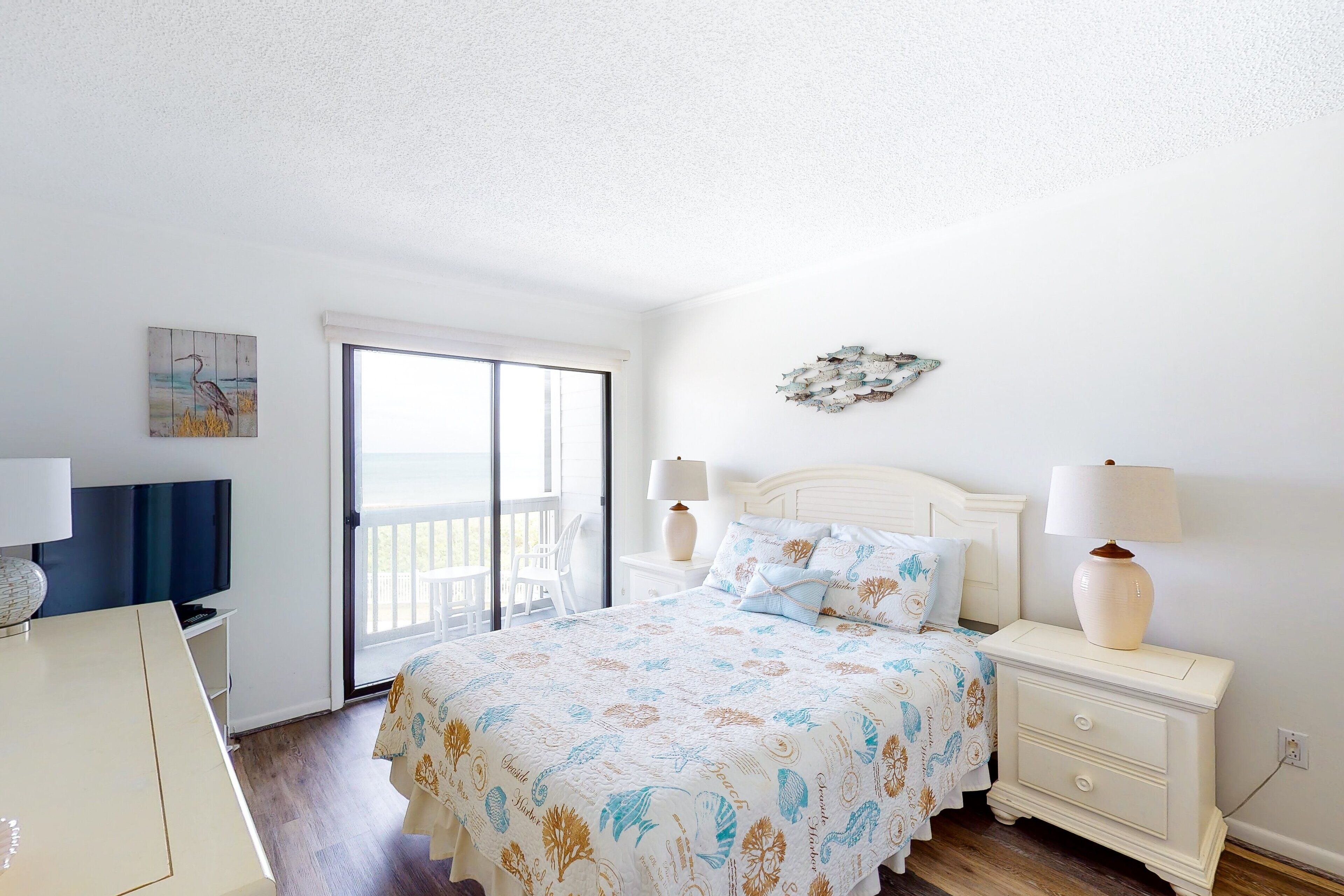 A bedroom with a bed, bedside lamps, a painting, a window, and a view of the outdoors.