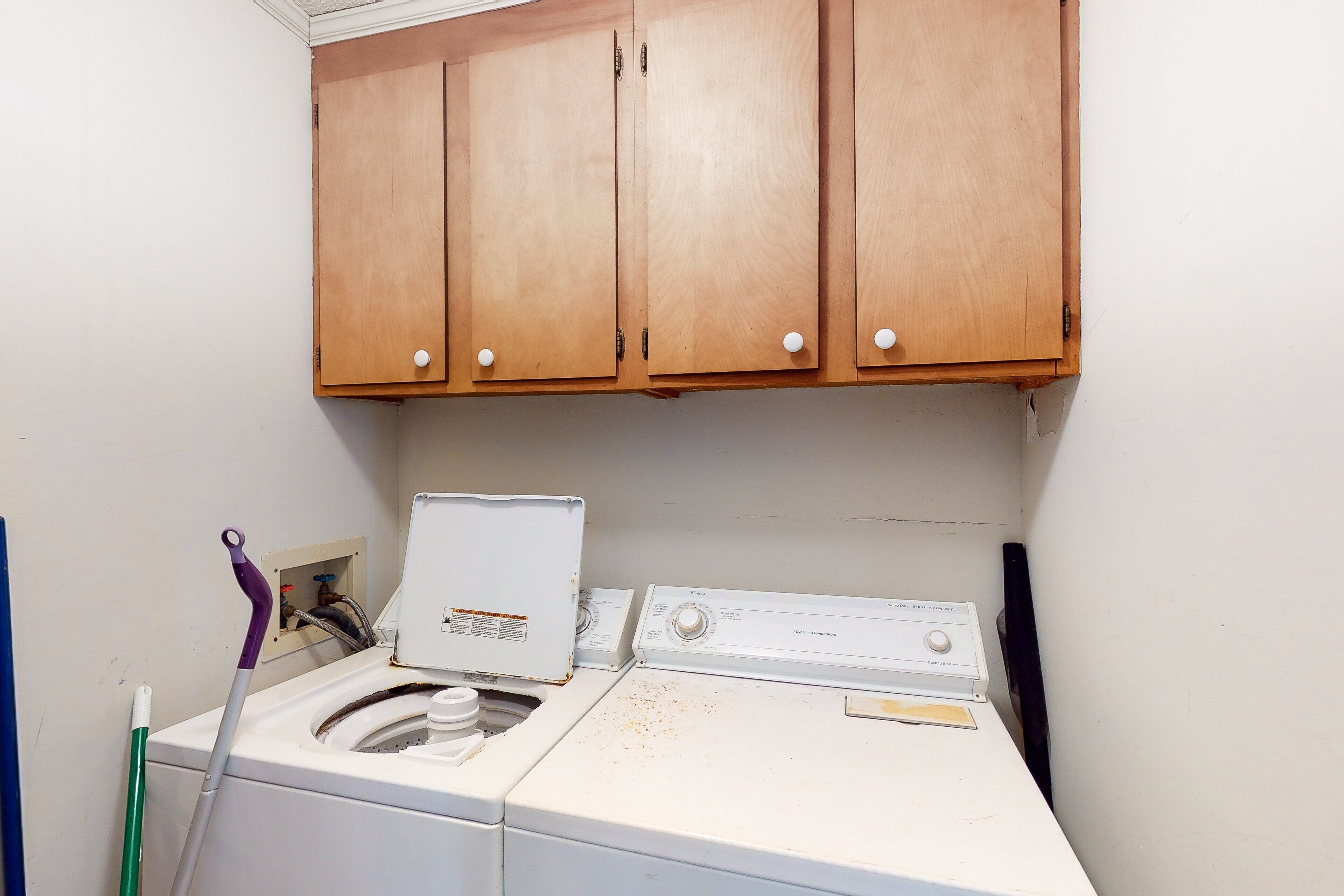 A laundry room with a washing machine, a dryer, and wooden cabinets above.