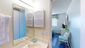 Une salle de bain équipée d’un lavabo, d’un miroir, d’une serviette et d’une chaise dans la pièce adjacente.