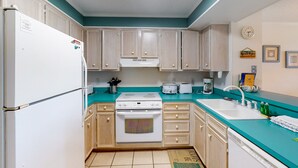 Una cocina con armarios de madera clara, un refrigerador blanco, una estufa y un lavamanos.