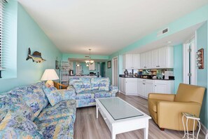 A living room with a sofa, a coffee table, and a chair. There is a kitchen area with cabinets and a countertop. - Oceanfront, First-Floor Condo with Balcony, Ocean View & Shared Pools/Tennis (Atlantic Beach)