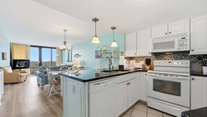 A kitchen with white cabinets, a microwave, an oven, and a dining area with a table and chairs. - Oceanfront, First-Floor Condo with Balcony, Ocean View & Shared Pools/Tennis (Atlantic Beach)