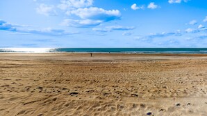 A wide sandy beach with footprints and a person walking in the distance.