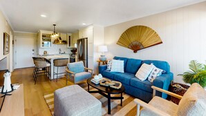 A modern living room with a blue sofa, a coffee table, and a dining area with chairs and a kitchen in the background.