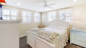 A bedroom with a bed, a nightstand, a lamp, a ceiling fan, and large windows. - Kellum Cottage: Spacious oceanfront home, large deck, beach access (Atlantic Beach)