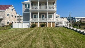 A multi-story building with a balcony on each floor, a fenced yard, and a clear blue sky. - Kellum Cottage: Spacious oceanfront home, large deck, beach access (Atlantic Beach)