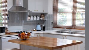 A kitchen with white cabinets, a wooden countertop, a gas stove, a sink, and a window with blinds. - Pear Tree Cottage - Apollo Bay (Apollo Bay)