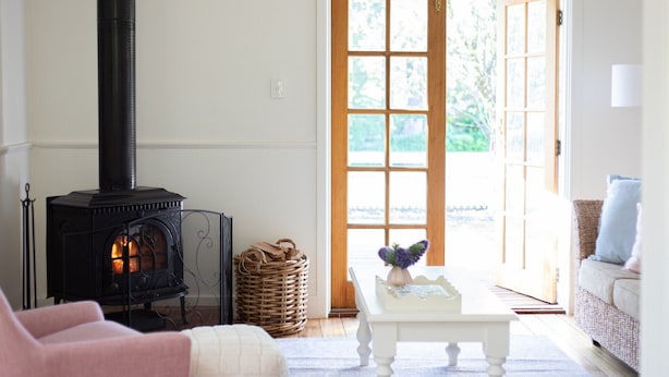 A cozy living room with a black wood-burning stove, wicker baskets, a white coffee table, and a wicker sofa. - Pear Tree Cottage - Apollo Bay (Apollo Bay)