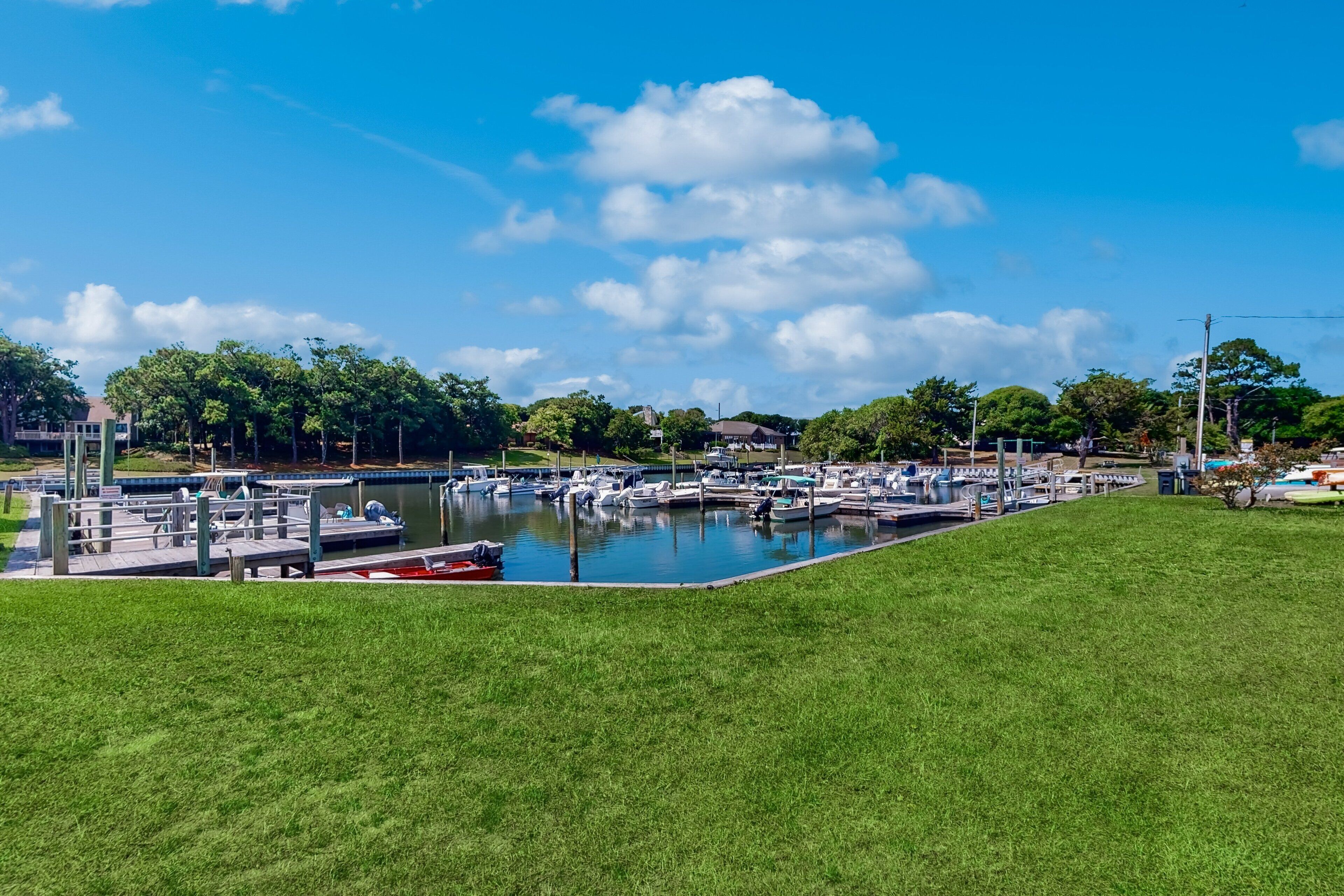A marina with boats docked, a grassy area in the foreground, and buildings in the background.