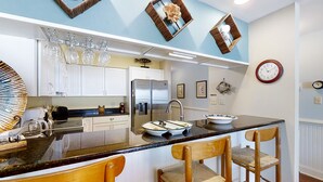 A kitchen with a central island, bar stools, a refrigerator, and a clock on the wall.