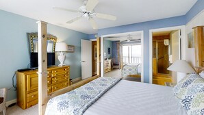A bedroom with a bed, dresser, TV, and a ceiling fan.