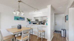 A modern kitchen with white cabinets, a wooden dining table, and a hanging light fixture.