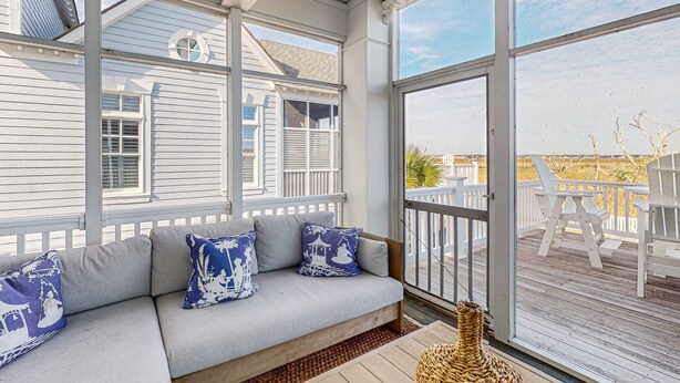 A covered porch with a cushioned seating area, large windows, and a view of the beach. - Soundside Serenity: Perfect Beach Getaway with Water Views, Shared Pool (Atlantic Beach)