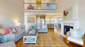 A spacious living room with a high ceiling, a fireplace, and a dining area in the background. - Soundside Serenity: Perfect Beach Getaway with Water Views, Shared Pool (Atlantic Beach)