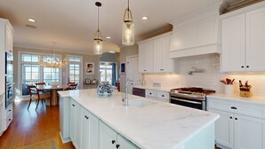 A spacious kitchen with white cabinetry, a large island with a sink, and pendant lighting. - Soundside Serenity: Perfect Beach Getaway with Water Views, Shared Pool (Atlantic Beach)